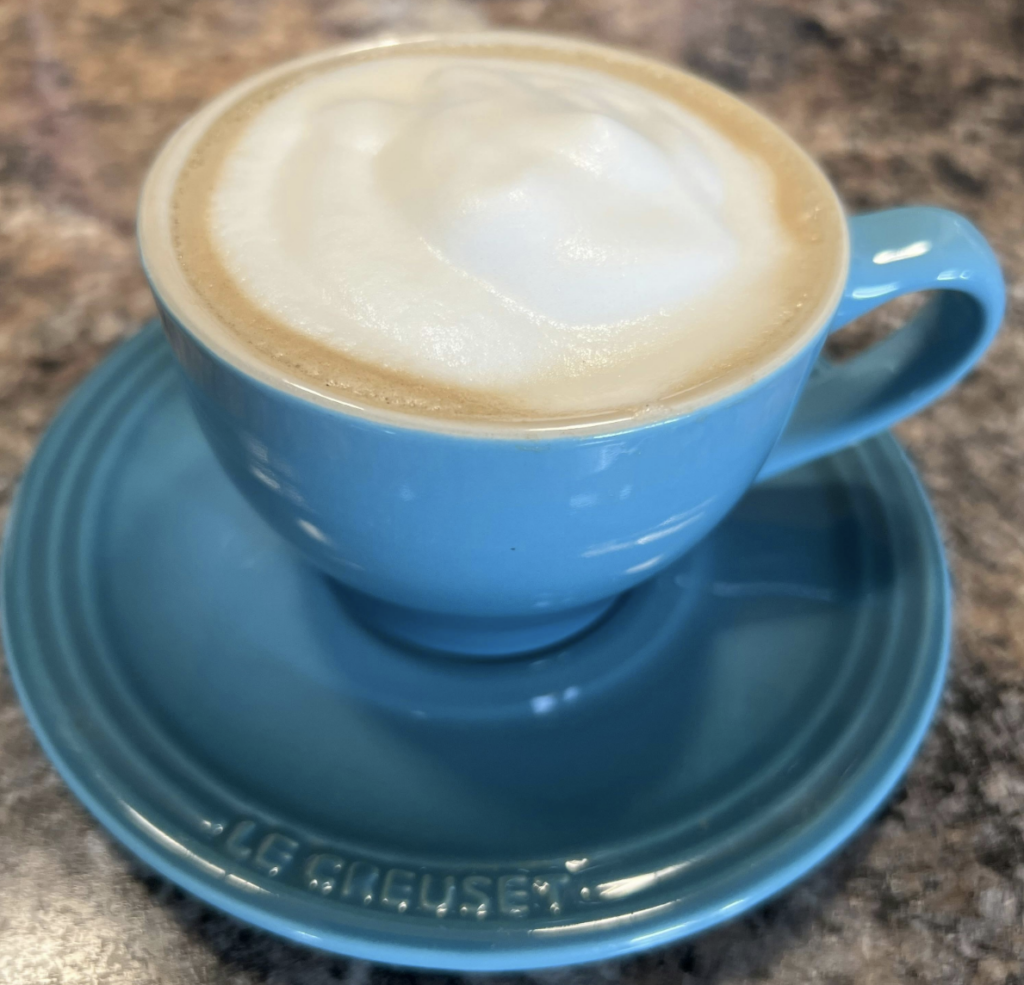 Blue cup with frothy cappuccino on saucer.