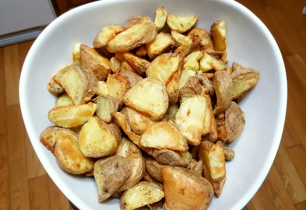 Bowl of roasted potato wedges on table.