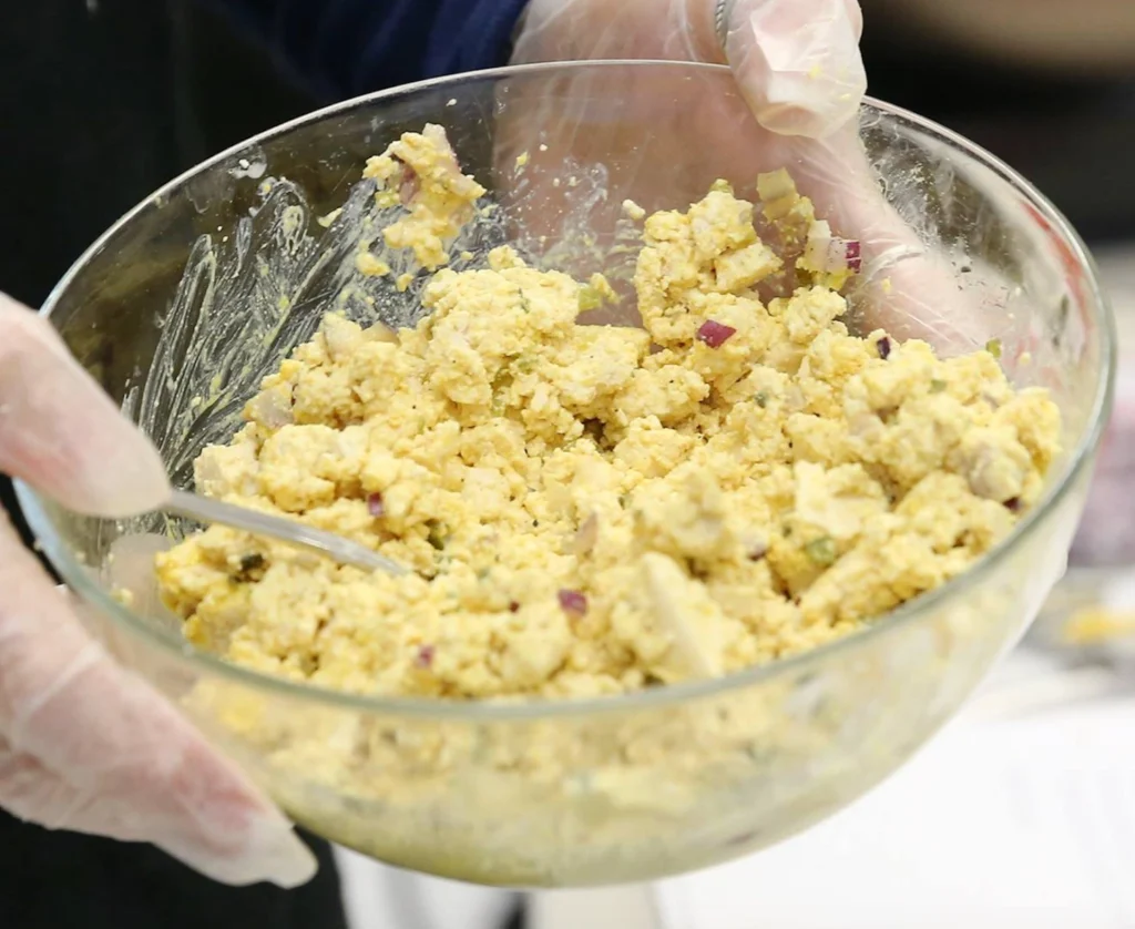 Person mixing egg salad in glass bowl.