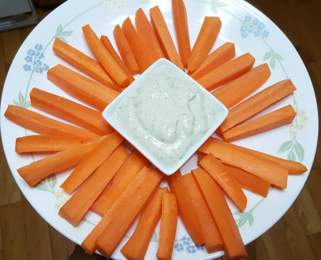 Carrot sticks with dip on floral plate.