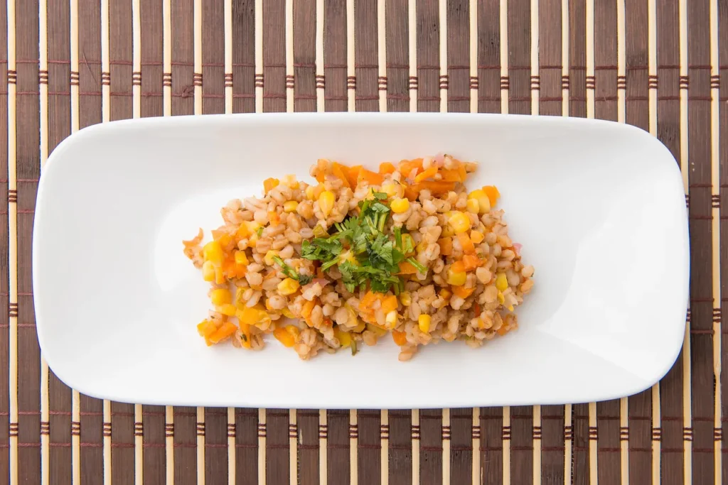 Barley salad with vegetables on white plate.