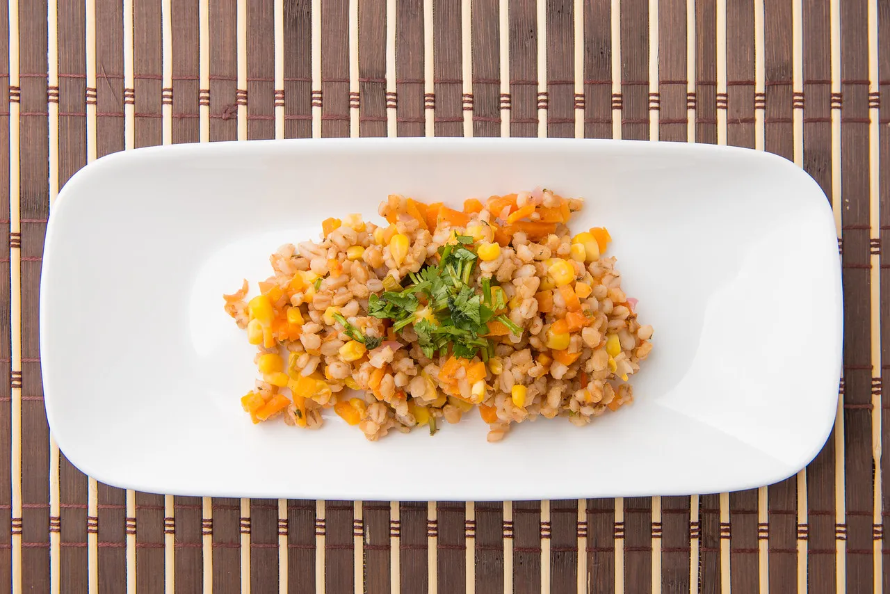 Barley salad with vegetables on white plate.