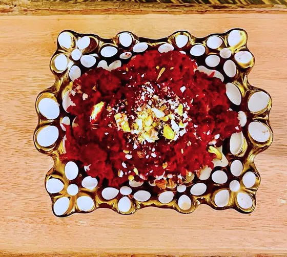 Red dessert garnished with nuts in decorative bowl.