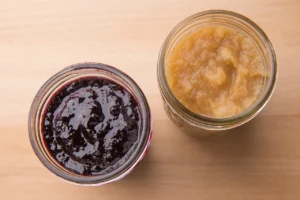 Two jars of fruit jam on table.