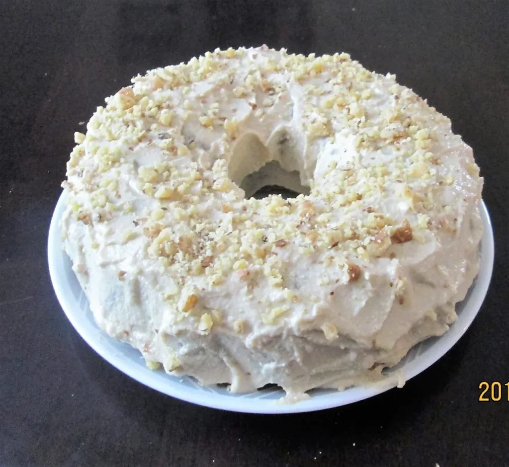 Frosted bundt cake with chopped nuts topping.