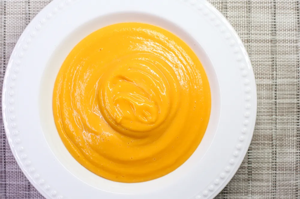 Creamy orange soup in white bowl.