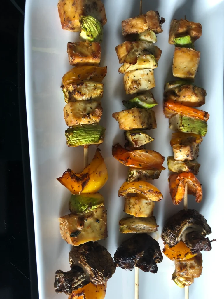 Grilled vegetable skewers on white plate.