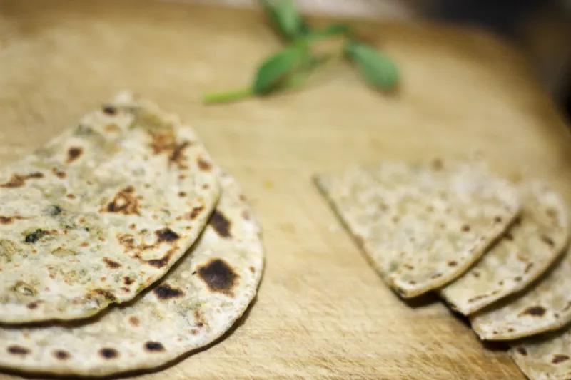 Flatbreads on wooden board with herbs.