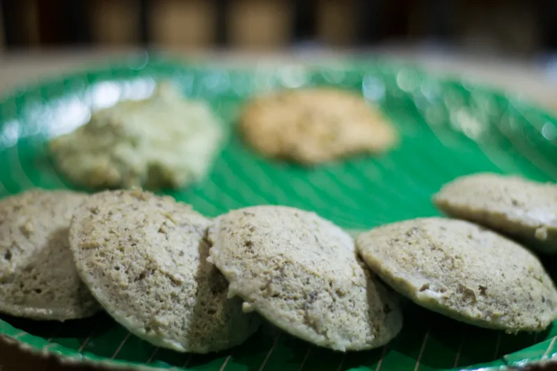 Idlis with chutneys on a green plate.