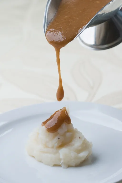 Gravy pouring onto mashed potatoes on plate.