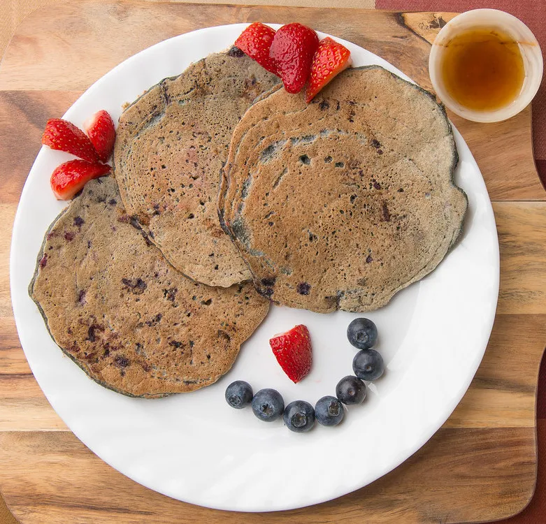 Pancakes with strawberries, blueberries, and syrup.
